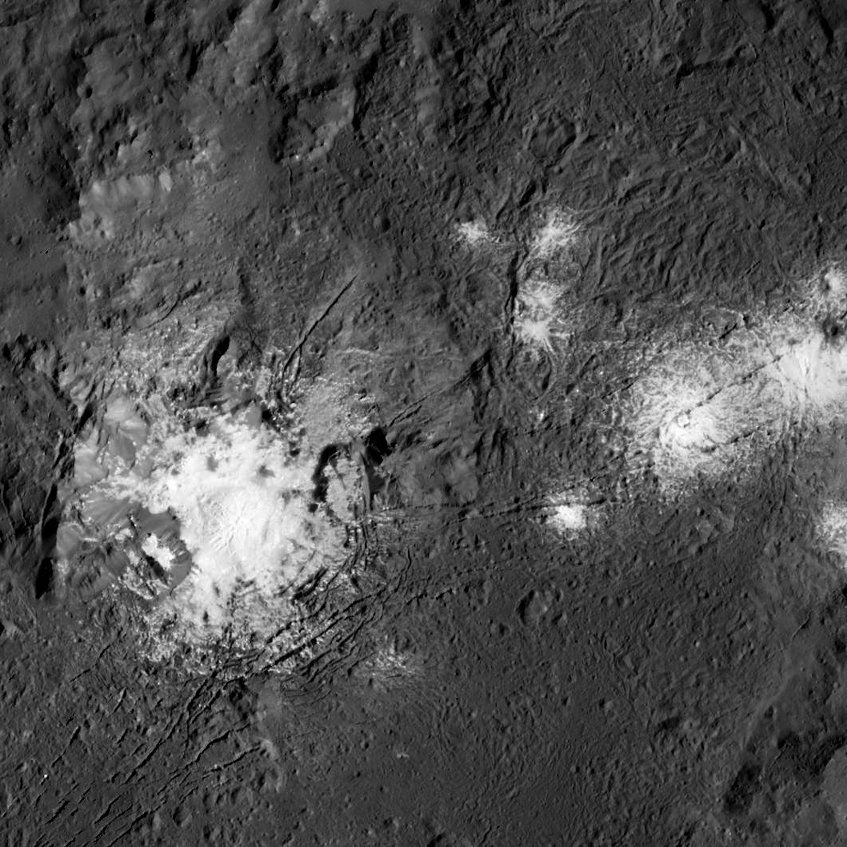 Occator ist der größte Krater auf Ceres und verfügt über die auffälligsten hellen Flecken Alternativ: Eine graue Landschaft, darin ein heller Fleck, rechts davon einige weitere Flecken, wie verplemperte Milch